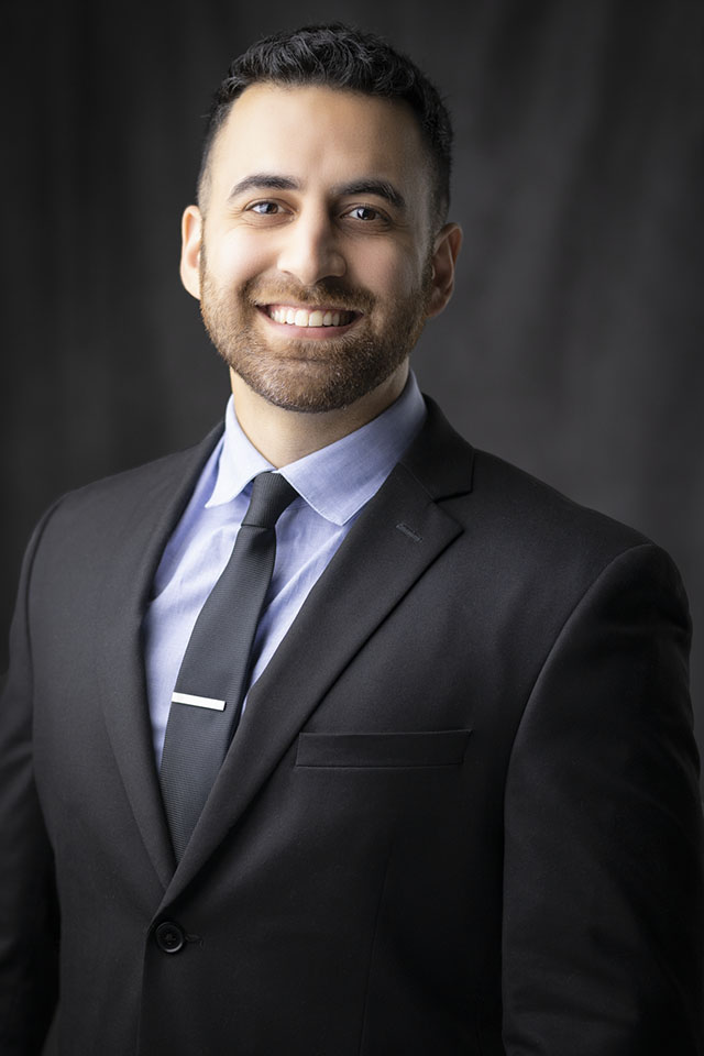 Studio headshot of a smiling man in a dark suit and tie