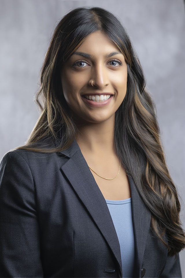 Studio headshot of a smiling woman in a dark blazer against a gray backdrop